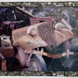 Vieille Citroën Traction rouillée au milieu d'une casse, entourée de ferraille, dans une bordure faite de pièces mécaniques, écrous et boulons.