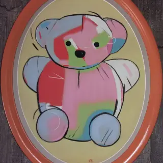 Ours en peluche assis, fait de pièces roses, bleues et vertes, sur un fond jaune, dans un médaillon ovale cerclé d'orange.